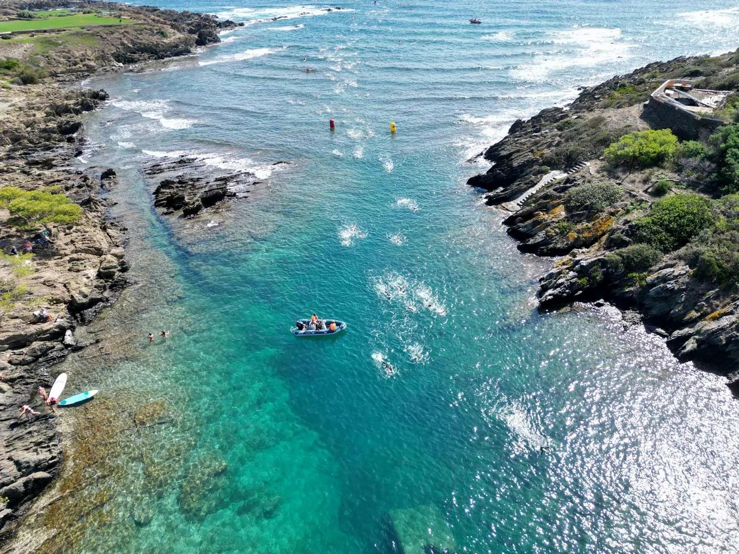 Swimmers and a support boat in a rocky cove during a Marnaton race